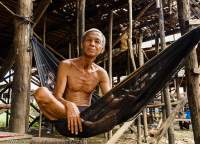 CAMBODIA, Siem Reap, Man in hammock beneath house on stilts, in seasonally-flooded village beside Tonle Sap lake.