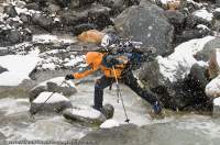 INDIA, Uttaranchal, Govind National Park. Trekker/skier fording Ruinsara river in snowstorm.