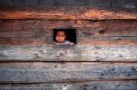 NEPAL, Himalaya, Mt Everest region. Curious child peers from wooden window, Lukla village.
