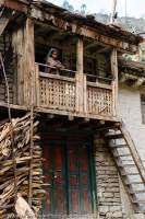 NEPAL, Mugu. Woman on verandah of house in small village.