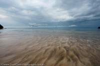 Ripples in beach sand at low tide, with storm clouds over Santubong Peninsula beyond, Bako National Park, Sarawak, Malaysia.