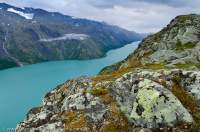 NORWAY, Oppland, Jotunheimen National Park. Lichen-covered rocks above Gjende lake, coloured by glacial silt suspended in water, Knutshoe & Leirungsdalen valley beyond.